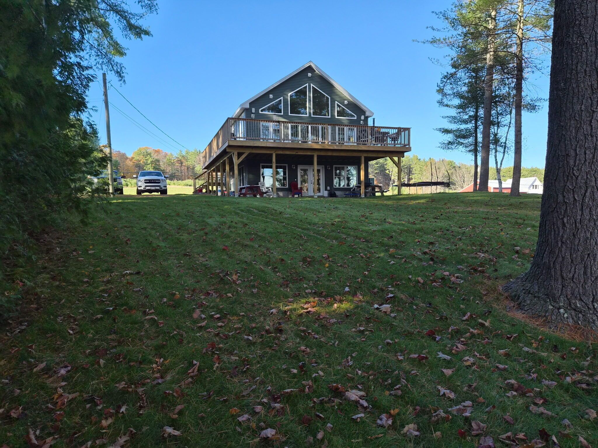 A large, two-story wooden cabin with a balcony, surrounded by a grassy yard and trees.