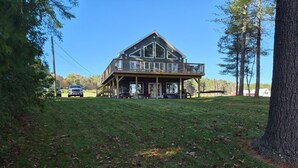 Une grande cabane en bois à deux étages, dotée d’un balcon, entourée d’une cour verdoyante et d’arbres.