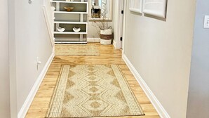 A hallway with a patterned rug, wooden flooring, and a shelving unit with decorative items. - EXCEPTIONAL, CONTEMPORARY 2BD/1BA  4 miles from MAYO (Rochester)