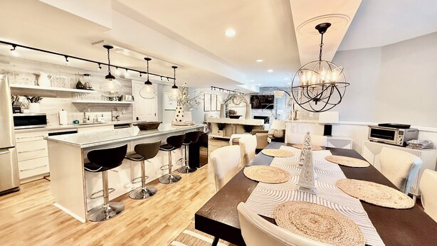 A modern kitchen with a central island, bar stools, and a dining area with a long table and chairs. - EXCEPTIONAL, CONTEMPORARY 2BD/1BA  4 miles from MAYO (Rochester)