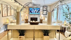 A modern living room with a fireplace, a television mounted on the wall, and decorative vases on a central console. - EXCEPTIONAL, CONTEMPORARY 2BD/1BA  4 miles from MAYO (Rochester)