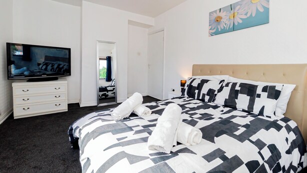 A hotel room with a bed, a television, a dresser, and a painting on the wall.
