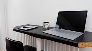 A laptop on a black desk with a notebook and a patterned mug.