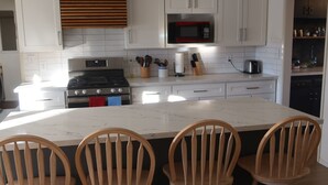 Una cocina moderna con armarios blancos, una isla central con taburetes, estufa, microondas y tostadora.