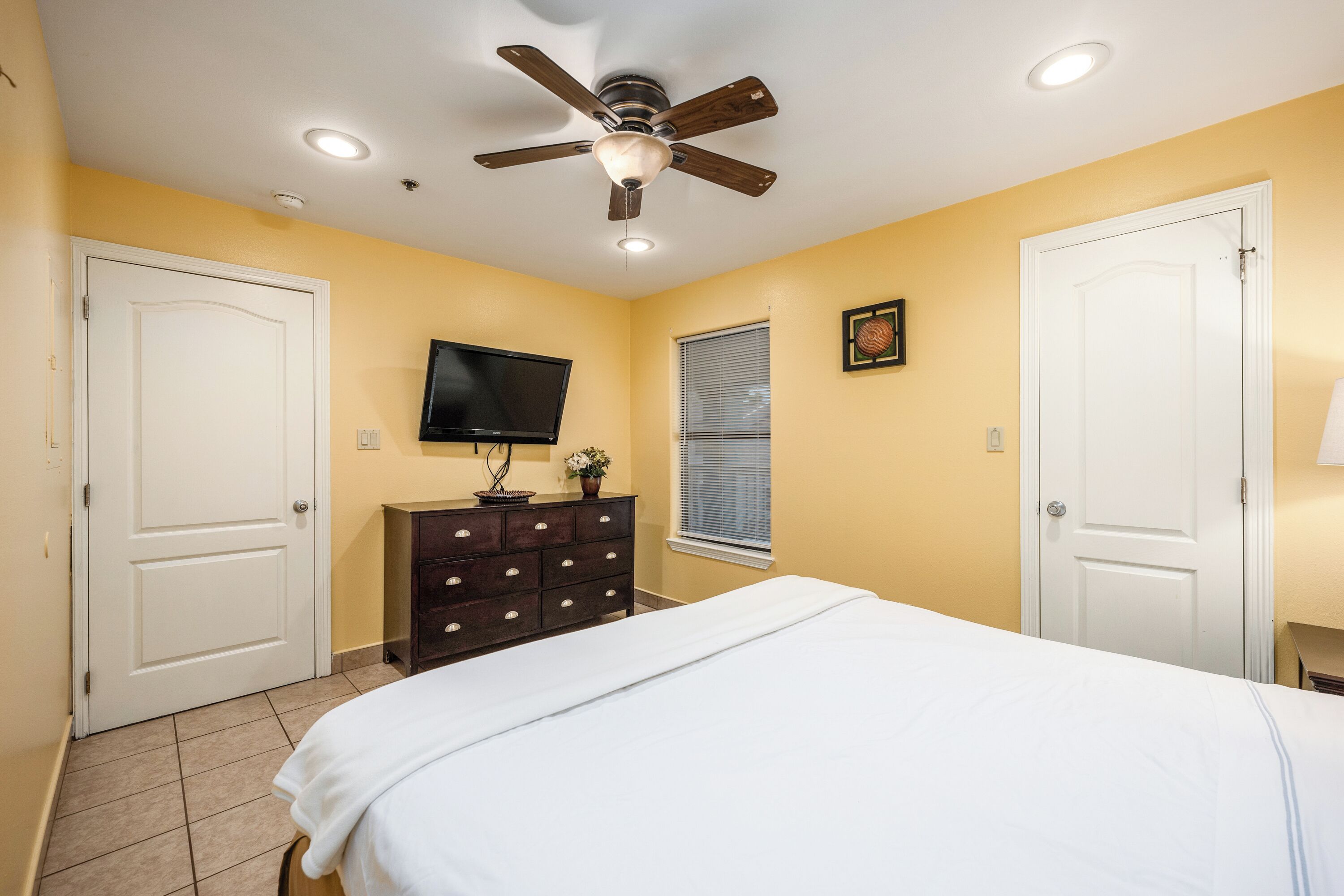 A bedroom with a bed, a dresser, a ceiling fan, a TV, and two doors.