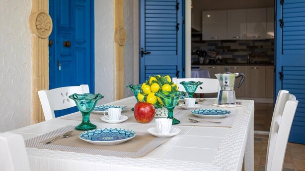 A dining table set with white chairs, blue and green glassware, and a fruit bowl. - [Shell House] AC|Wi-Fi|P private|BBQ (Castelvetrano)