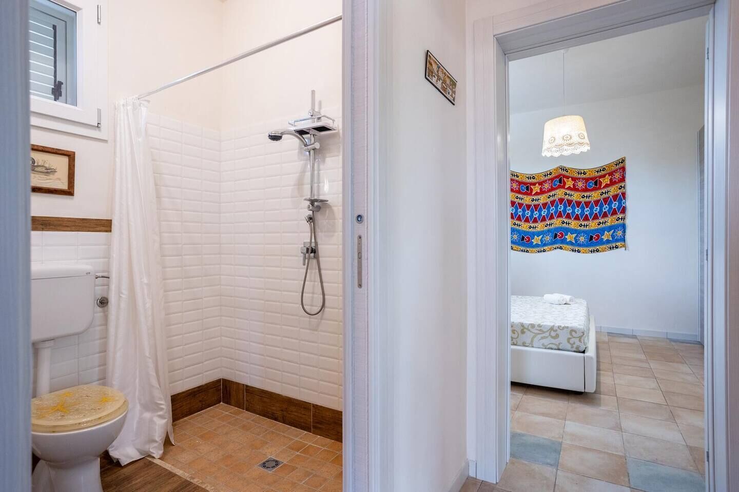Une salle de bain avec douche et toilettes, et une chambre adjacente avec un lit.