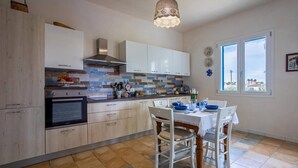 A modern kitchen with white cabinets, a built-in oven, and a dining area with a table set for two. - [Shell House] AC|Wi-Fi|P private|BBQ (Castelvetrano)