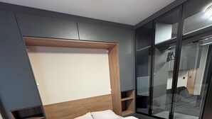 Une chambre moderne avec un grand lit, des étagères intégrées, une armoire en verre et un appareil de climatisation visible.