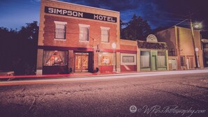 Das Simpson Hotel mit Ziegelaußenwand, einem markanten Schild und einem kleinen Anbau mit einem Schild, das eine Bank kennzeichnet.