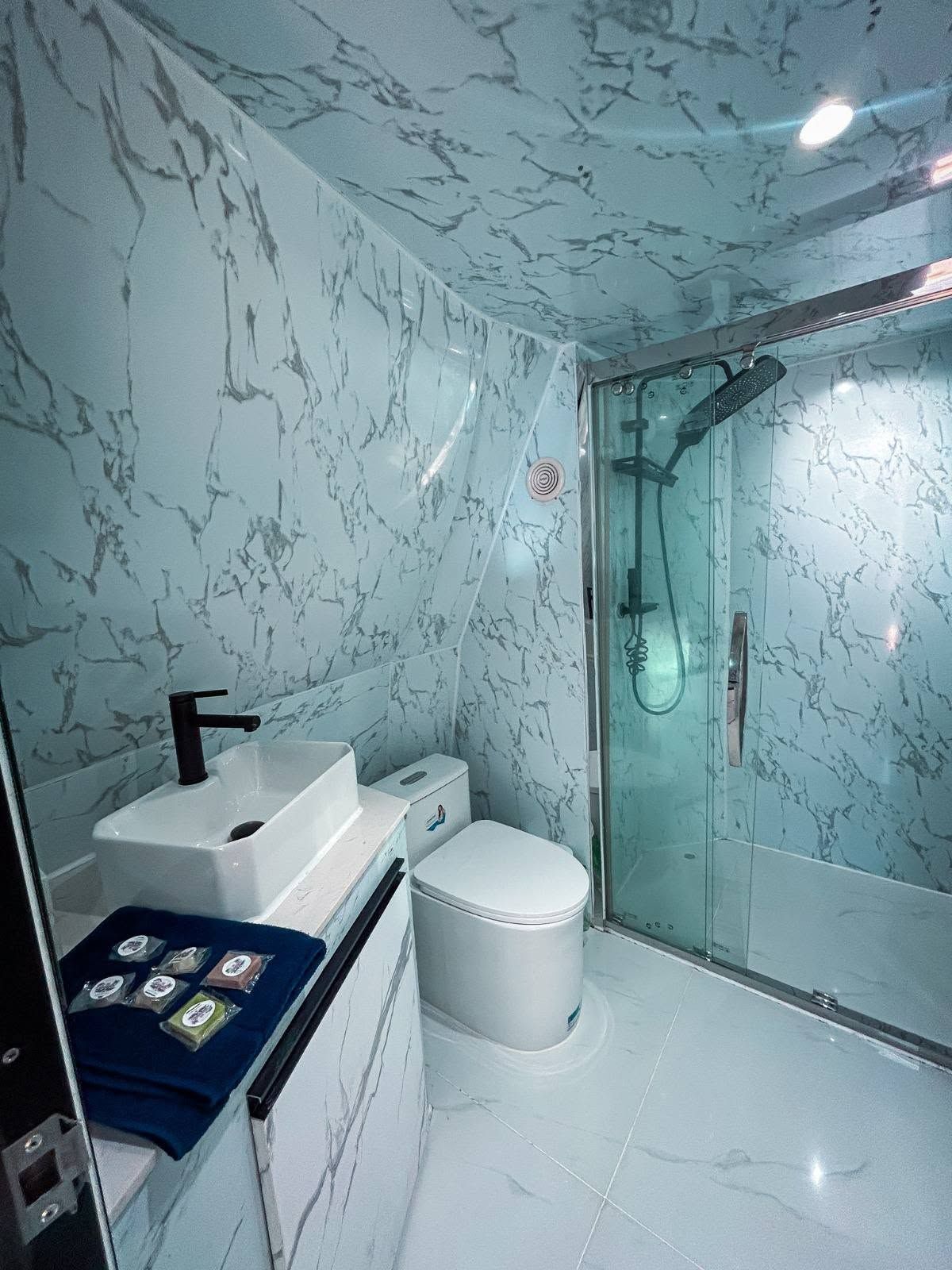 Un baño con pared de mármol, lavamanos, inodoro y cabina de ducha con mampara de vidrio.