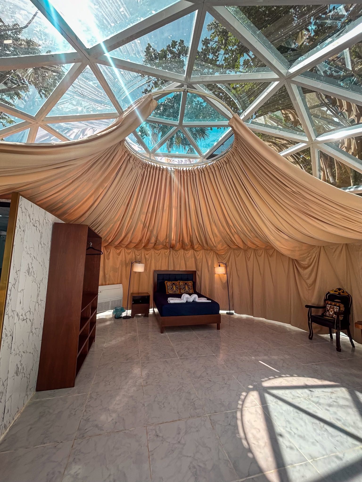 A room with a bed, a chair, a lamp, and a large glass ceiling.