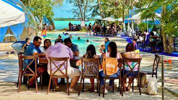A group of people seated at a table by a poolside, with a view of the pool and the ocean in the background.