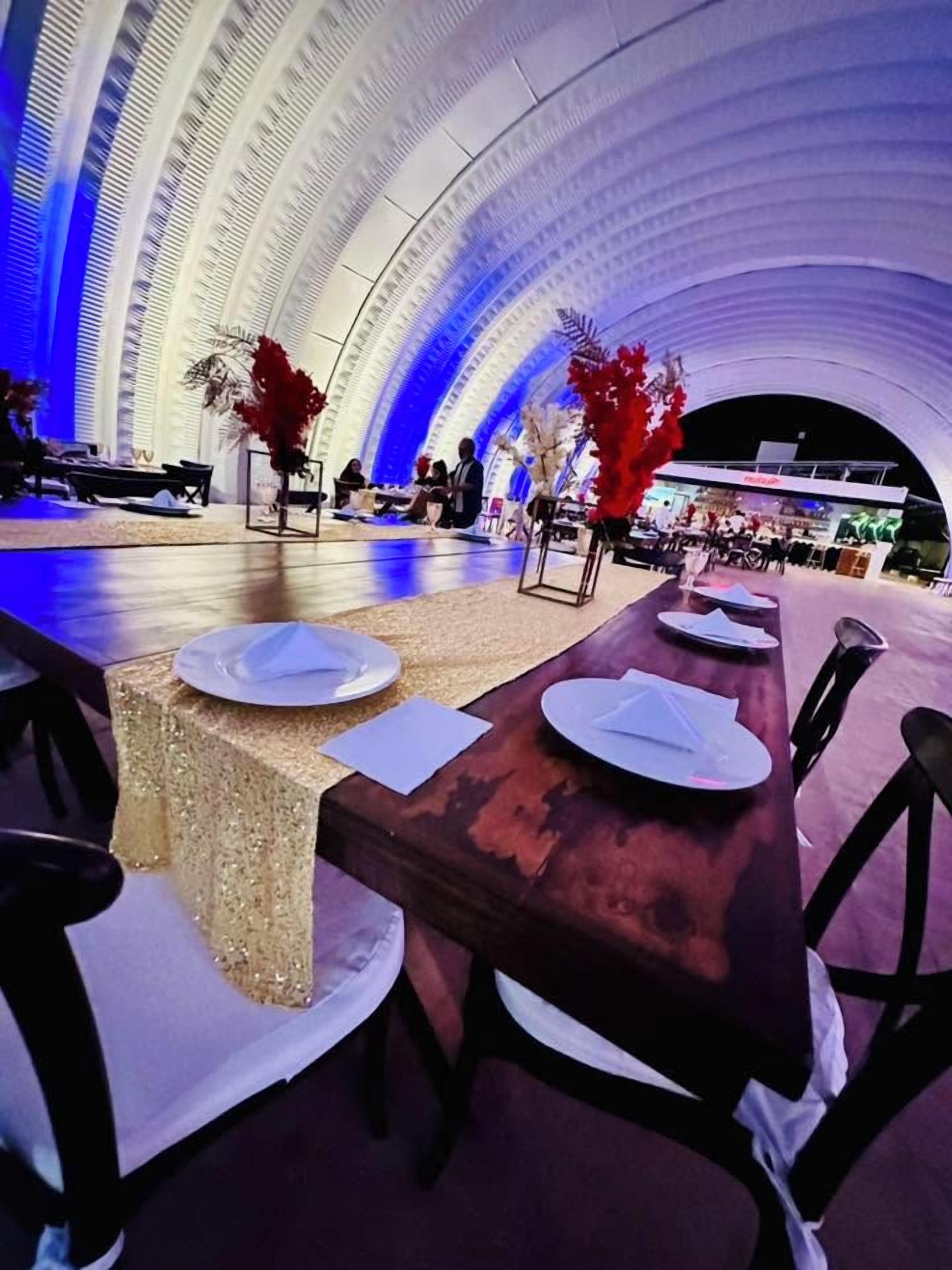Uma longa mesa de jantar com cadeiras, posta com pratos e guardanapos, em um espaço amplo e interno com teto alto e design arquitetônico curvo.