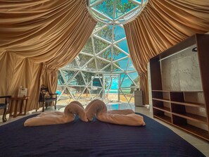 Une chambre dotée d’un grand lit, d’une télévision et offrant une vue à travers une fenêtre aux formes géométriques.