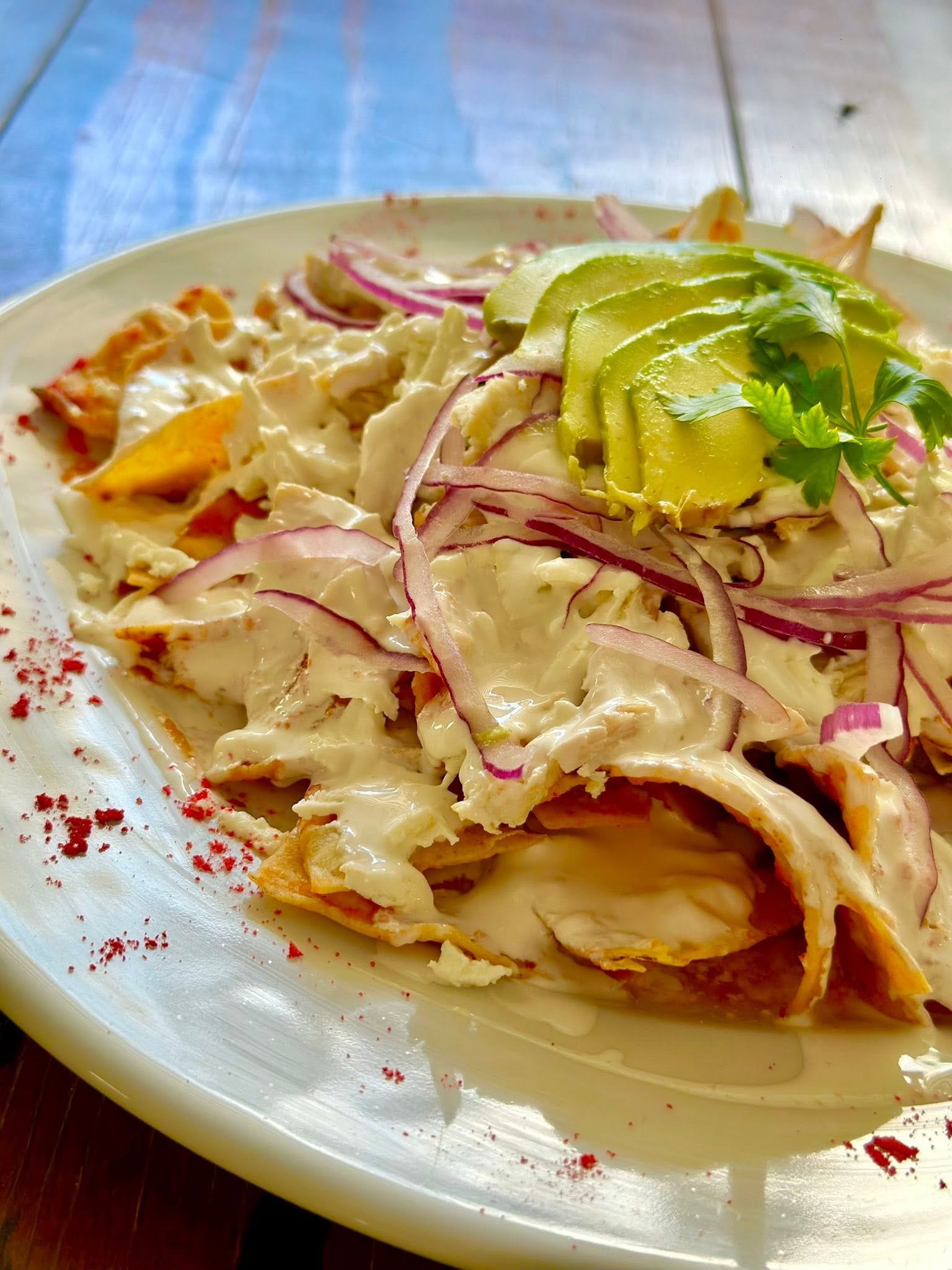 Un plato de comida con carne en rodajas, cebollas y salsa cremosa, adornado con hierbas.