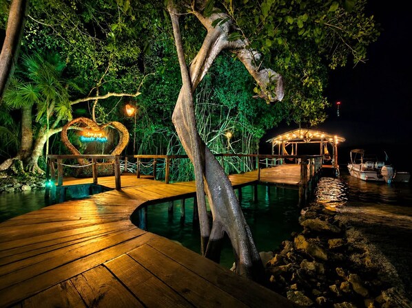 Um deck de madeira que leva a uma piscina cercada por vegetação exuberante e uma instalação de luz em formato de coração.