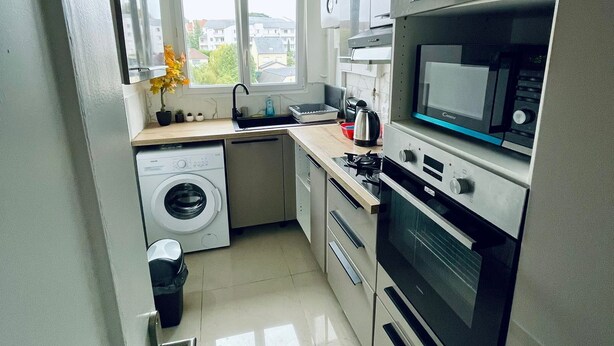 Een moderne keuken met een wasmachine, oven, magnetron en een raam met uitzicht op gebouwen.