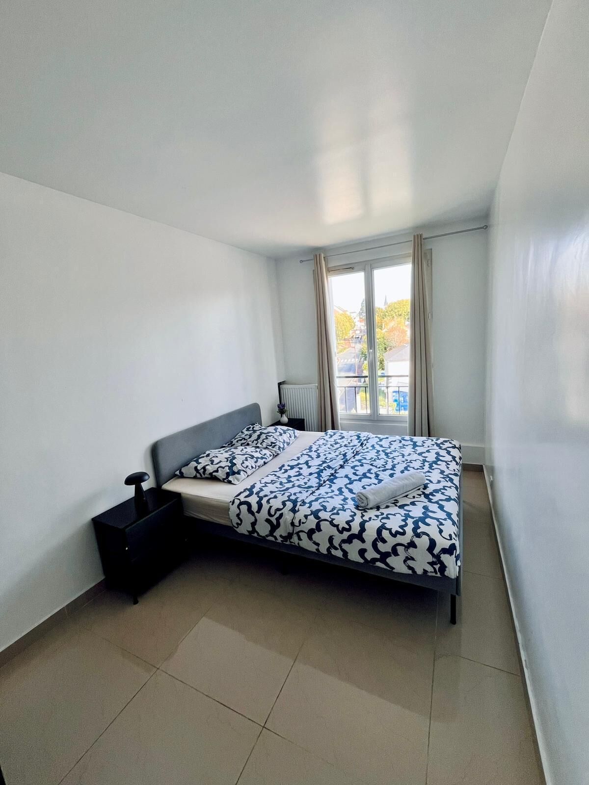 Ein Schlafzimmer mit einem Bett, einem Nachttisch, einem Heizkörper und einem Fenster mit Vorhängen.
