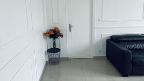 Een kamer met een witte deur, een zwarte leren bank en een kleine ronde tafel met een bloevas.