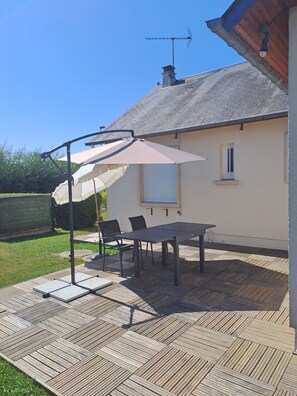 Une terrasse extérieure avec une table et des chaises, un grand parasol et une cheminée.