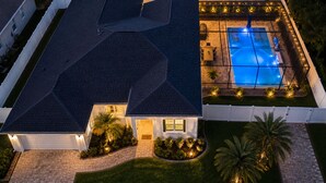 Une maison avec une piscine, une allée et un jardin bien aménagé à l’avant, avec un bon éclairage.