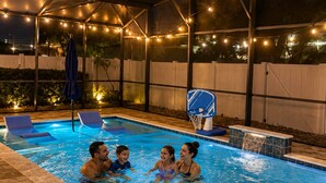 Une piscine extérieure équipée d’un panier de basketball, de chaises longues et de guirlandes lumineuses.