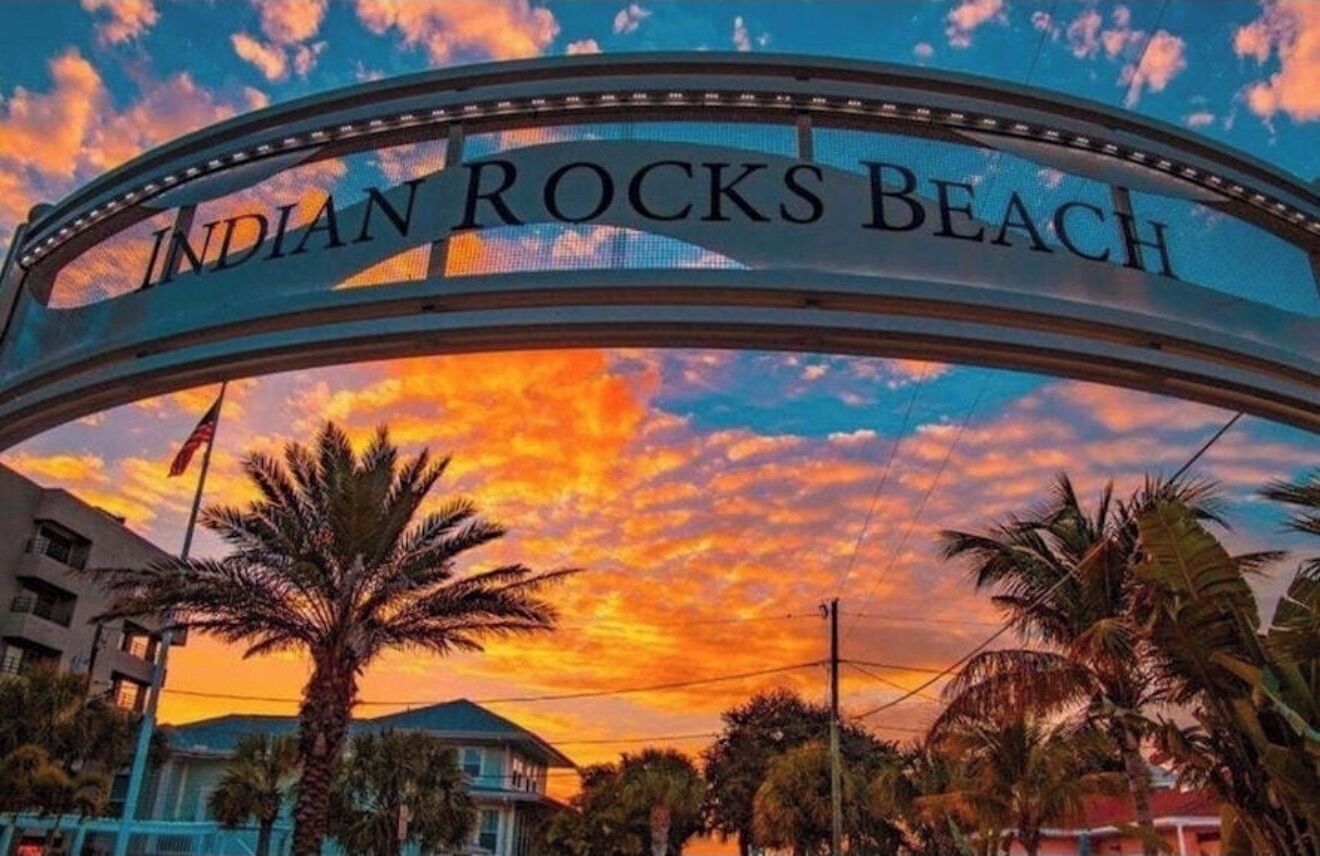 A sign reading 'INDIAN ROCKS BEACH' with palm trees and buildings in the foreground.