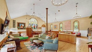 A spacious living area with a high ceiling, wooden flooring, and a mix of seating including sofas and a bench.