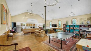 A spacious room with a ping pong table, wooden furniture, a kitchen area, and a bookshelf.