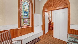 A wooden interior with a stained glass window, white doors, and a bench.