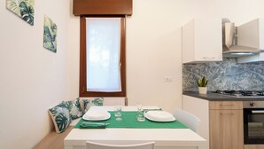 A modern kitchen with a dining area. It includes a table set for two, a window with blinds, and a stove. - Al Pettirosso: 15 min to Venice, 2 Double Bedrooms, Free Private Parking (Venezia)