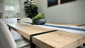 A wooden dining table with a black metal frame, a white and blue striped runner, and a potted plant on the table. - Clean Modern Apartment-75” SMART TV & Xbox (Payson)