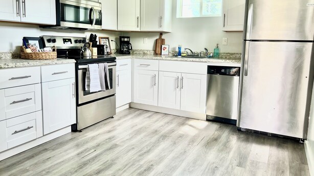 A modern kitchen with white cabinets, stainless steel appliances, and a wooden floor. - Clean Modern Apartment-75” SMART TV & Xbox (Payson)