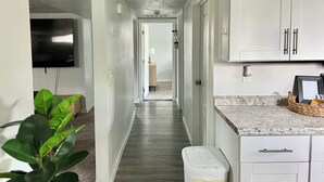 A narrow hallway with white cabinets, a TV mounted on the wall, and a plant in the foreground. - Clean Modern Apartment-75” SMART TV & Xbox (Payson)