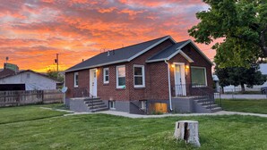 A brick house with a front porch, a garage, and a well-maintained lawn. - Clean Modern Apartment-75” SMART TV & Xbox (Payson)