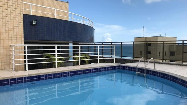 A swimming pool with a blue tiled edge, a white safety railing, and a building with a blue-tiled facade in the background. - Flat Atlantic Ocean - Praia de Iracema (Fortaleza)