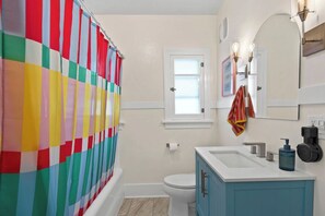 A bathroom with a colorful striped shower curtain, a white toilet, a blue vanity with a sink, and a mirror with wall-mounted lights. - Manito Craftsman with Fire Pit (Spokane)