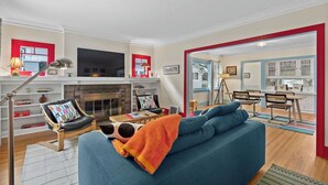 A modern living room with a sofa, a fireplace, a television, and a dining area. - Manito Craftsman with Fire Pit (Spokane)
