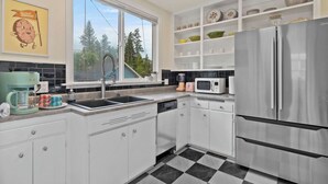 A modern kitchen with white cabinets, a stainless steel refrigerator, a microwave, and a sink. - Manito Craftsman with Fire Pit (Spokane)