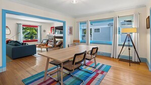 A modern living room with a wooden dining table, blue-framed windows, and a colorful rug. - Manito Craftsman with Fire Pit (Spokane)