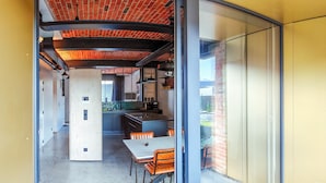 A modern kitchen with a central island, a dining area with orange chairs, and a glass partition. - La Camuche by Hélène Dutrieu (Tournai)