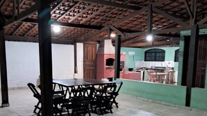 Zona pranzo all'aperto riparata, con forno a mattoni, tavolo e sedie, e parete verde sullo sfondo.