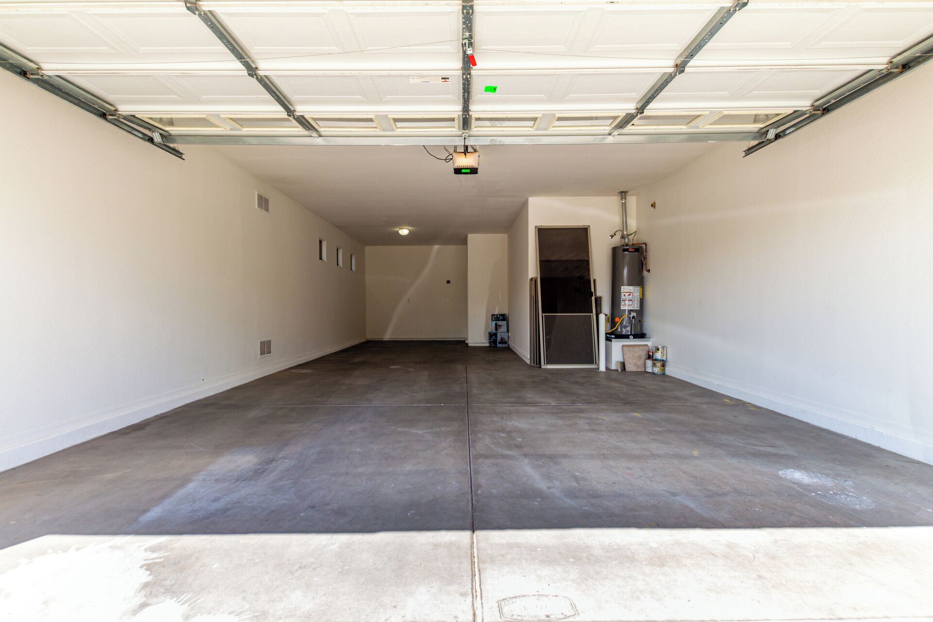 Un garage propre et dégagé, avec un sol en béton, un plafond équipé de néons et un chauffe-eau visible sur le côté droit.