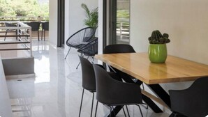 Un comedor moderno con una mesa de madera y sillas negras, un cactus en maceta verde y vistas al exterior.