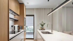 Una cocina moderna con armarios de madera, encimera blanca y un amplio ventanal con cortinas.