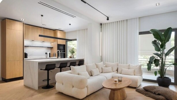 Una sala de estar moderna con un sofá seccional color beige, una mesa de centro redonda de madera y una zona de bar con taburetes.