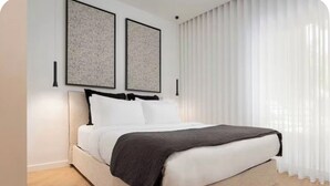 Un dormitorio moderno con cama, ropa de cama blanca y dos cuadros enmarcados en la pared.
