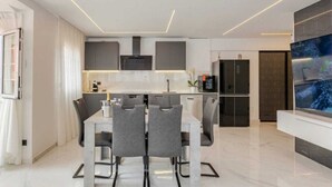 Cocina moderna con comedor, que incluye una isla grande, armarios grises y un televisor de pantalla plana.