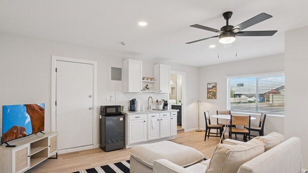 A modern living room with a sofa, a TV, and a kitchen area with cabinets and a refrigerator. - Chic & Cozy Studio | King Bed + Sleeper (Tempe)